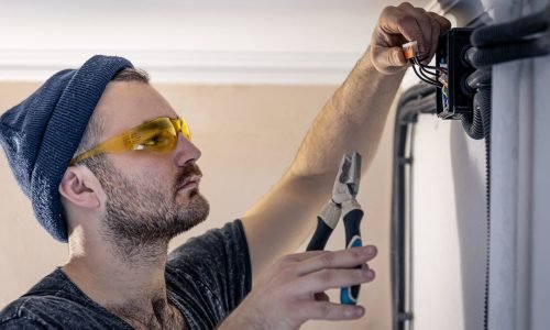 Attractive male electrician repairing an outlet, installing an outlet indoors.